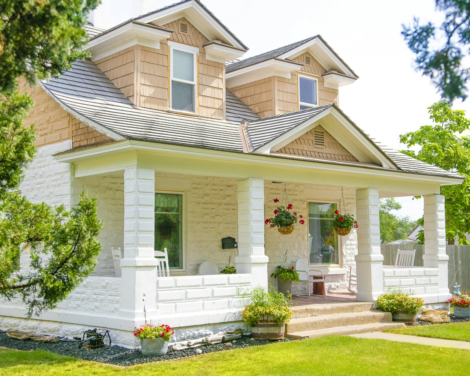 A white two-storey home with a wide front porch, hanging flower baskets and a mown lawn.